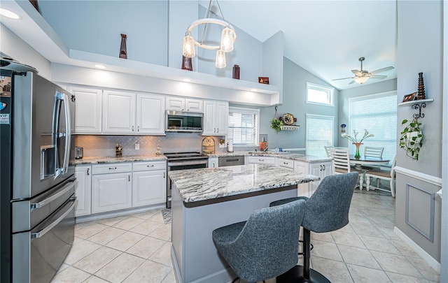 kitchen featuring a breakfast bar area, decorative light fixtures, stainless steel appliances, light stone countertops, and white cabinets