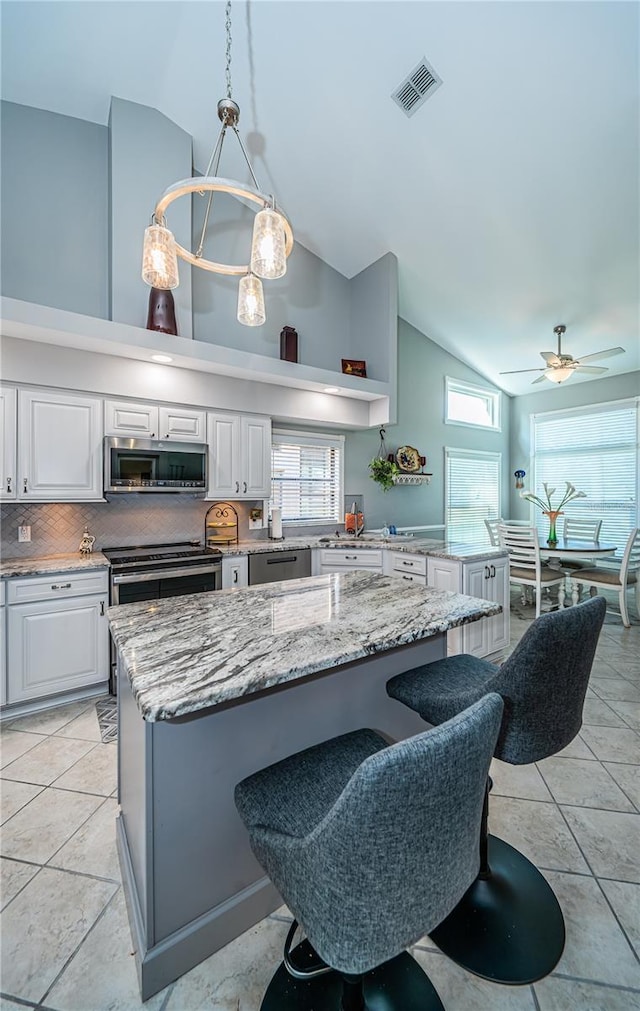 kitchen with appliances with stainless steel finishes, a center island, tasteful backsplash, light stone countertops, and decorative light fixtures