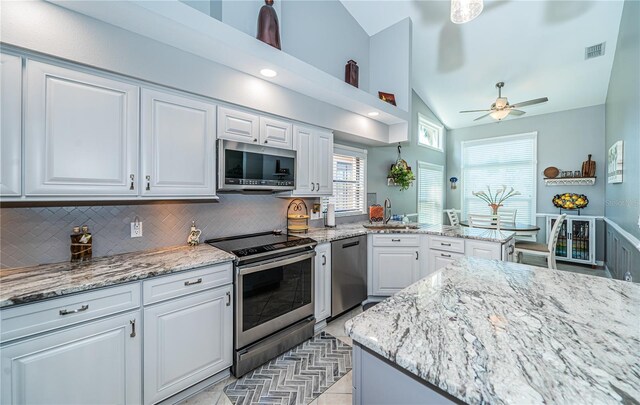 kitchen with vaulted ceiling, tasteful backsplash, white cabinets, stainless steel appliances, and light stone countertops