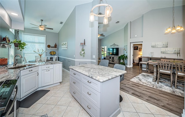 kitchen with ceiling fan with notable chandelier, white cabinetry, hanging light fixtures, a center island, and light stone countertops