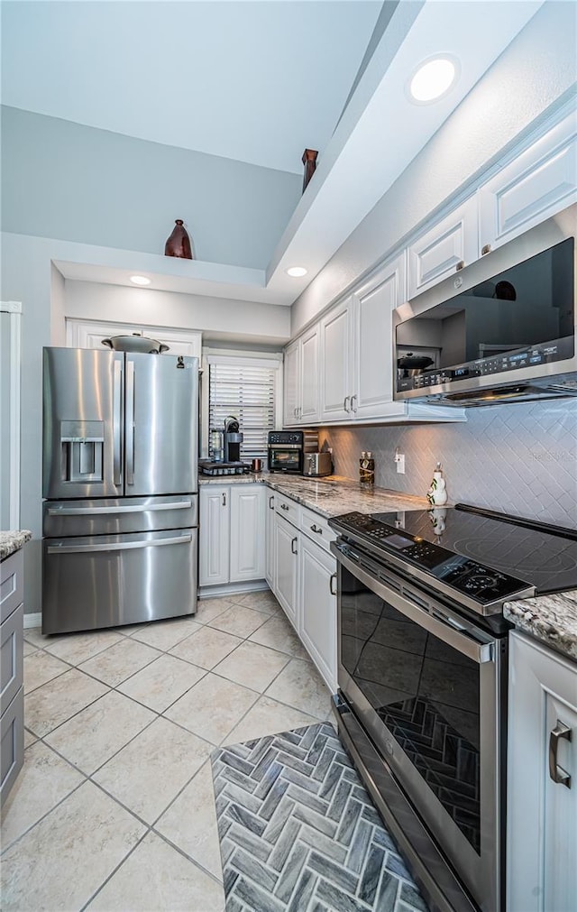 kitchen with appliances with stainless steel finishes, tasteful backsplash, white cabinets, light tile patterned floors, and light stone counters