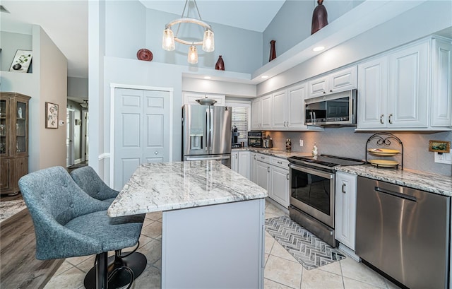 kitchen with appliances with stainless steel finishes, a center island, light stone countertops, white cabinets, and decorative light fixtures