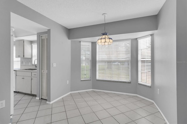 unfurnished dining area featuring a healthy amount of sunlight, sink, light tile patterned floors, and a textured ceiling