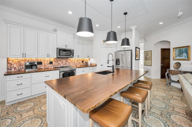 kitchen with a kitchen island with sink, white cabinets, sink, tasteful backsplash, and premium appliances