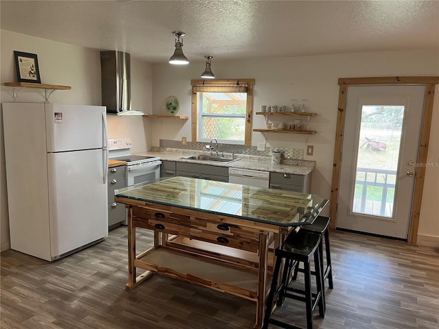 kitchen featuring white appliances, wall chimney range hood, decorative light fixtures, sink, and a healthy amount of sunlight