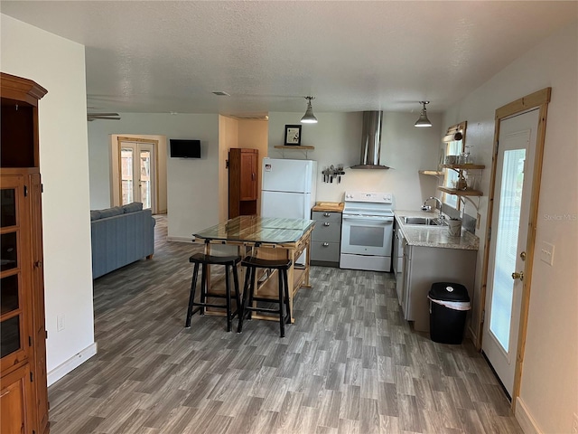 kitchen with white appliances, hanging light fixtures, wall chimney range hood, sink, and dark wood-type flooring