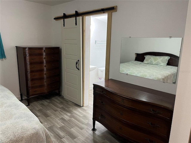 bedroom with hardwood / wood-style floors, ensuite bath, and a barn door