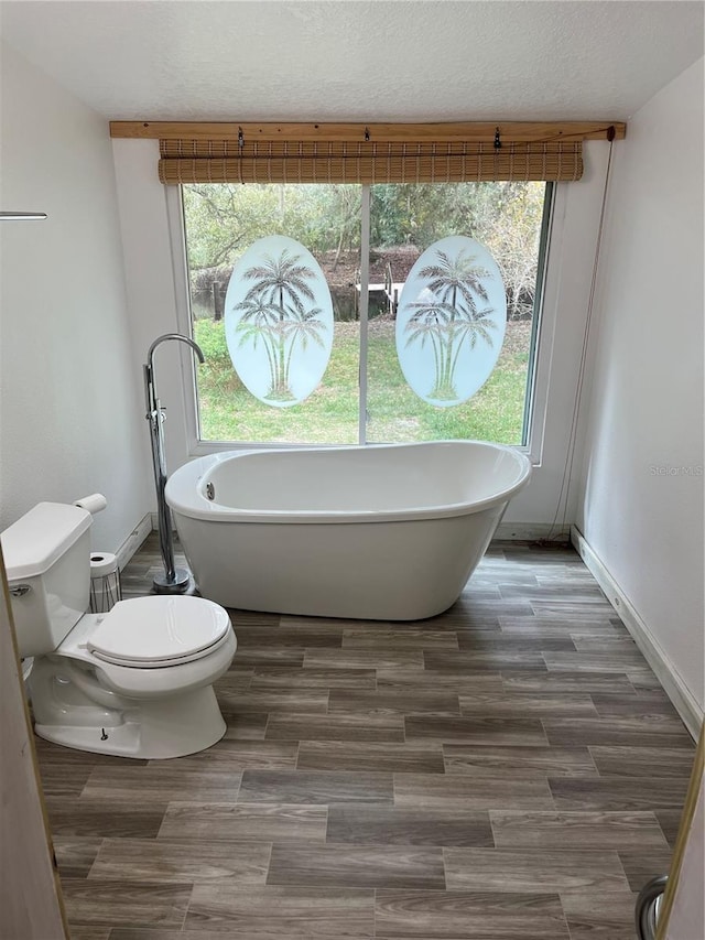 bathroom with a tub to relax in, toilet, and a healthy amount of sunlight