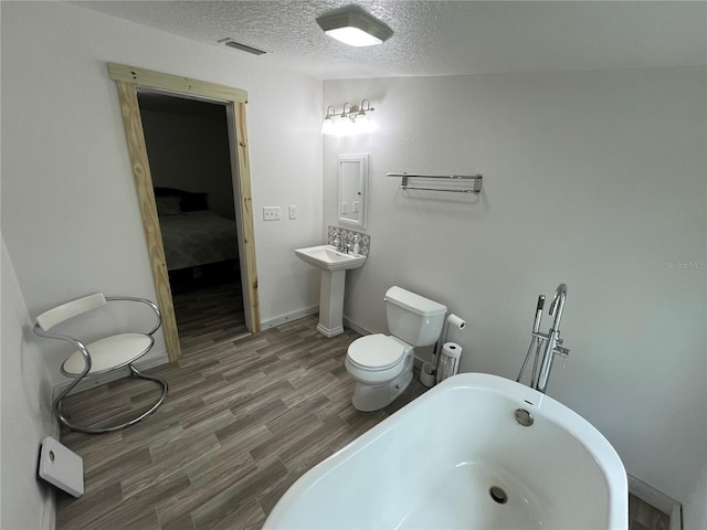 bathroom with a textured ceiling, a tub, sink, toilet, and hardwood / wood-style flooring