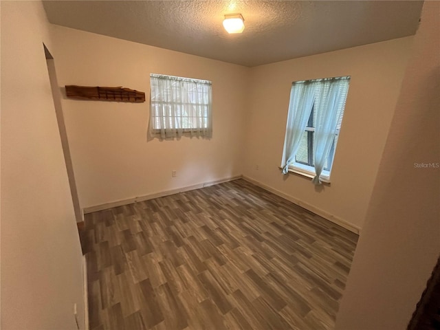 empty room featuring a textured ceiling, dark hardwood / wood-style floors, and a wealth of natural light