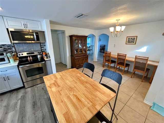 kitchen with pendant lighting, decorative backsplash, appliances with stainless steel finishes, a notable chandelier, and white cabinetry