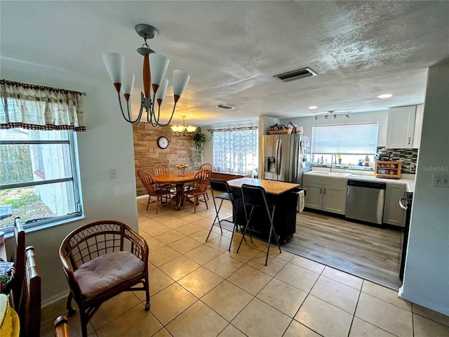 kitchen with appliances with stainless steel finishes, light tile patterned floors, decorative light fixtures, a notable chandelier, and white cabinets