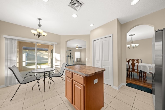 kitchen featuring ceiling fan with notable chandelier, a kitchen island, decorative light fixtures, and stainless steel refrigerator