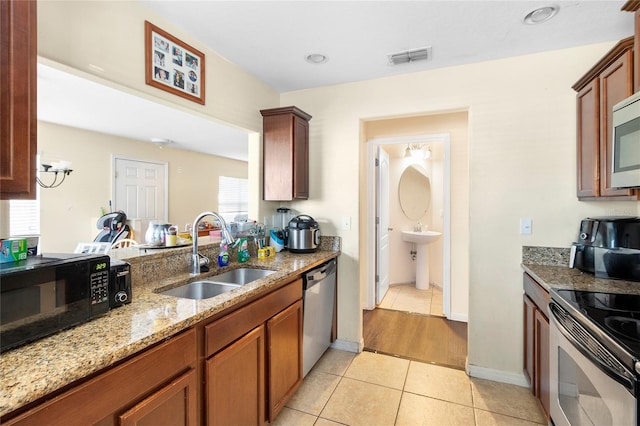 kitchen with light tile patterned flooring, stainless steel appliances, light stone countertops, and sink