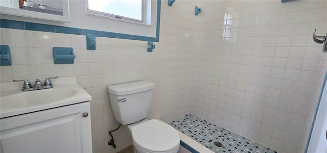 bathroom featuring tiled shower, vanity, toilet, and tile walls