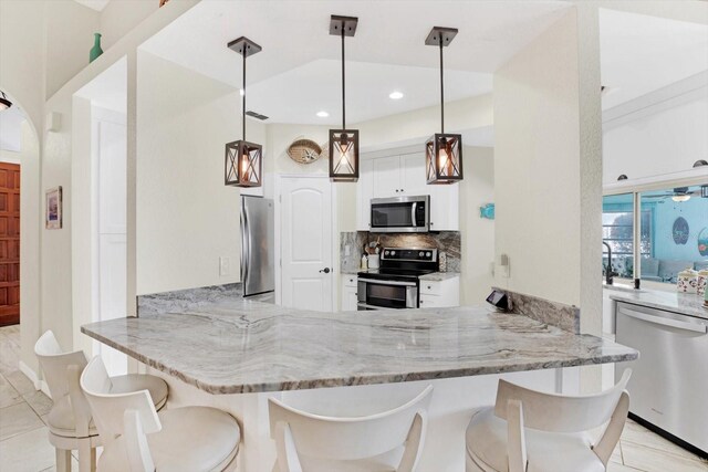 kitchen with kitchen peninsula, hanging light fixtures, a breakfast bar area, white cabinetry, and stainless steel appliances