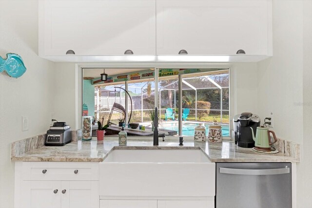 kitchen featuring stainless steel dishwasher, white cabinets, light stone countertops, and sink