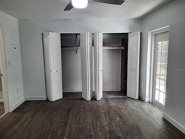 unfurnished bedroom featuring ceiling fan, dark hardwood / wood-style flooring, a textured ceiling, and two closets