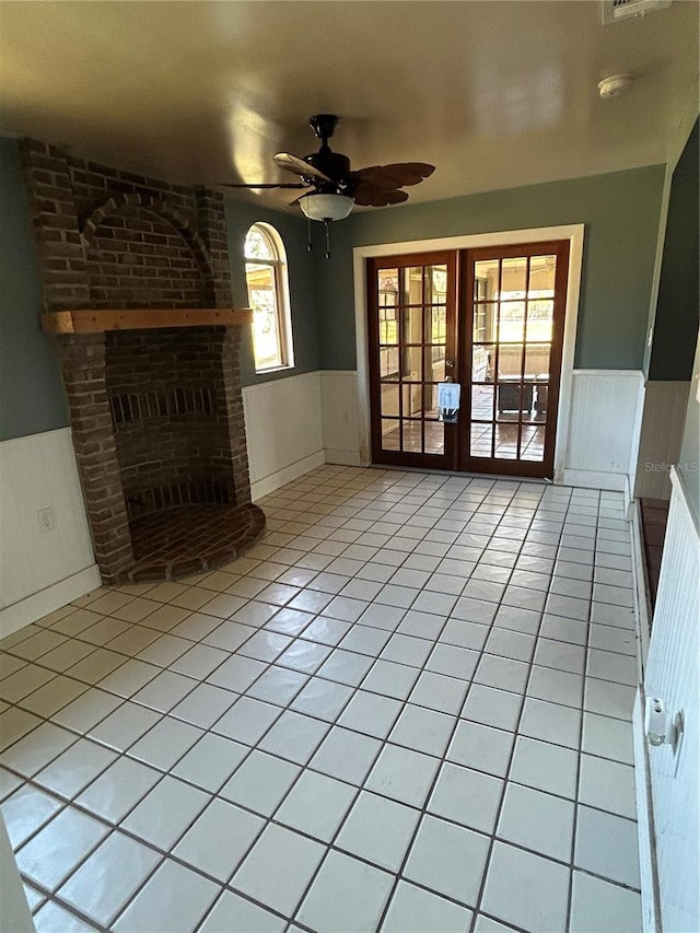 unfurnished living room with ceiling fan, french doors, a brick fireplace, and light tile patterned floors