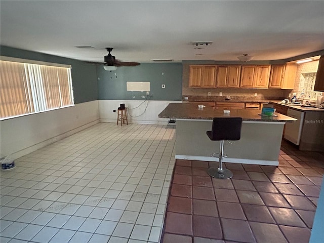 kitchen with a kitchen bar, a wealth of natural light, tile patterned floors, and ceiling fan