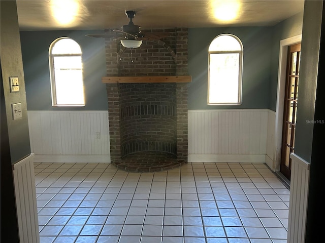 unfurnished living room with ceiling fan, a brick fireplace, and light tile patterned floors