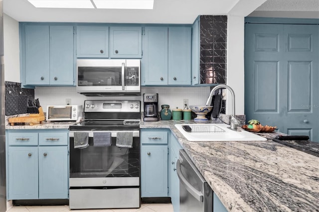 kitchen with appliances with stainless steel finishes, backsplash, sink, blue cabinetry, and light tile patterned floors