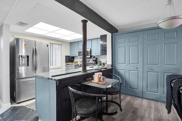 kitchen with dark hardwood / wood-style floors, blue cabinetry, a textured ceiling, kitchen peninsula, and stainless steel appliances