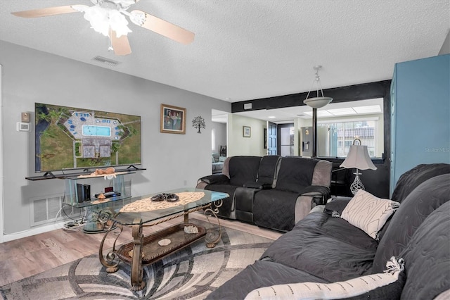 living room with ceiling fan, a textured ceiling, and light hardwood / wood-style flooring