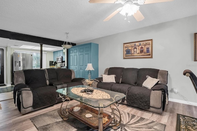 living room with ceiling fan, a textured ceiling, and light hardwood / wood-style flooring