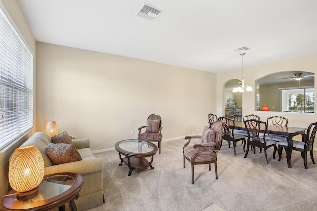 living area with ceiling fan with notable chandelier and light colored carpet