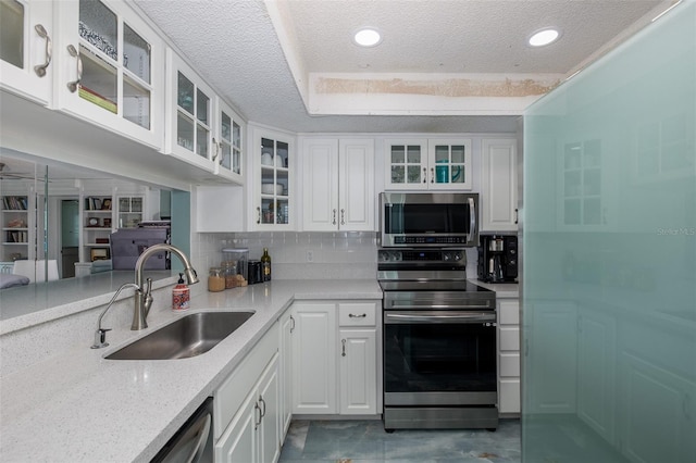 kitchen with stainless steel appliances, sink, white cabinets, a textured ceiling, and light stone countertops