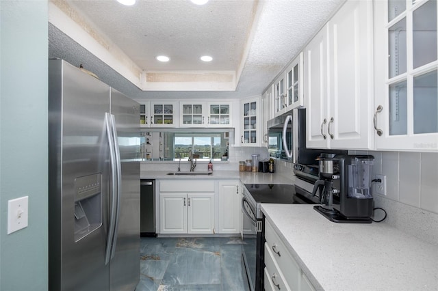 kitchen with stainless steel appliances, white cabinets, sink, and a tray ceiling