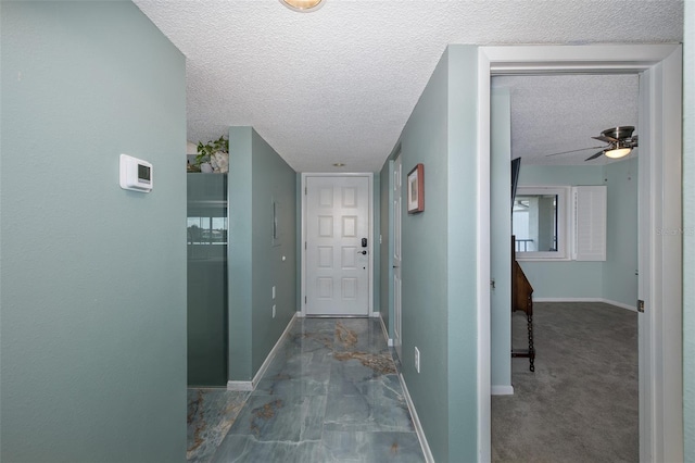 corridor featuring a textured ceiling and dark colored carpet