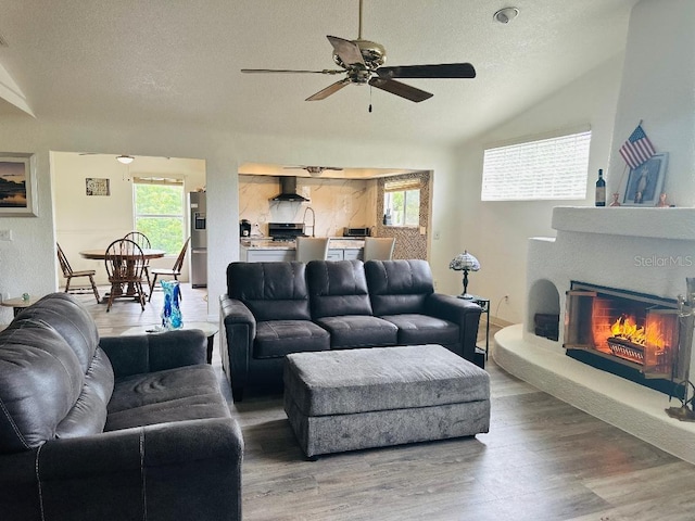 living room featuring hardwood / wood-style flooring, ceiling fan, lofted ceiling, and a textured ceiling