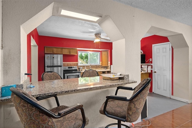 kitchen with ceiling fan, stainless steel appliances, a kitchen breakfast bar, kitchen peninsula, and a textured ceiling