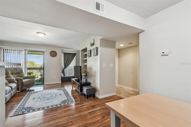 living room with built in shelves and dark hardwood / wood-style flooring