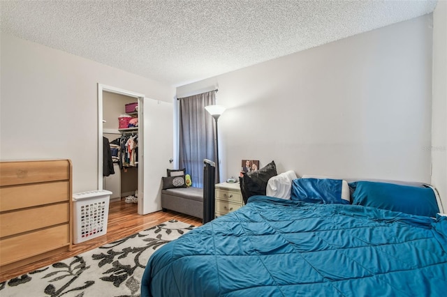 bedroom featuring a walk in closet, a textured ceiling, hardwood / wood-style flooring, and a closet