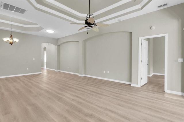 unfurnished living room with ceiling fan with notable chandelier, a tray ceiling, light hardwood / wood-style flooring, and ornamental molding