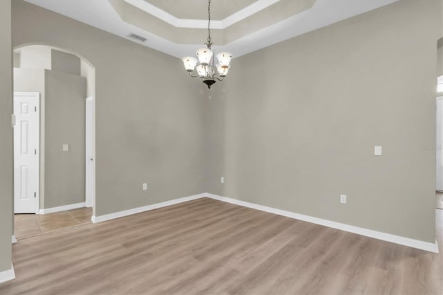 unfurnished room featuring a chandelier, light wood-type flooring, a raised ceiling, and crown molding