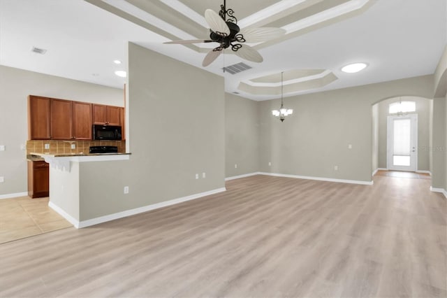 unfurnished living room featuring ceiling fan with notable chandelier, a raised ceiling, and light wood-type flooring