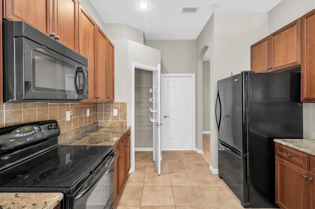 kitchen with tasteful backsplash, light stone counters, light tile patterned floors, and black appliances