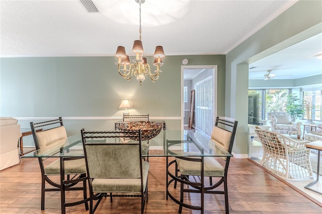 dining space with crown molding, ceiling fan with notable chandelier, wood-type flooring, and a textured ceiling