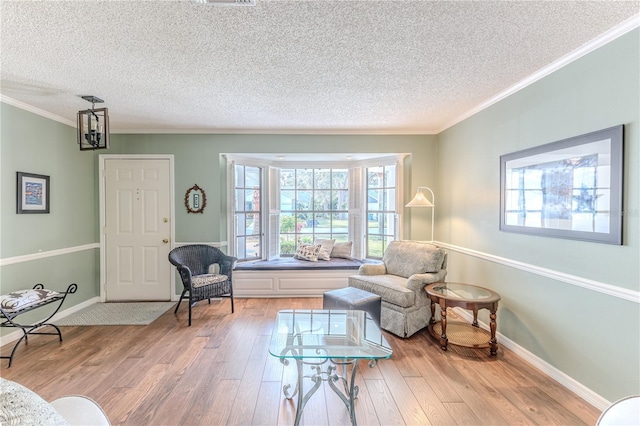 living area with a textured ceiling, light wood-type flooring, crown molding, and a chandelier