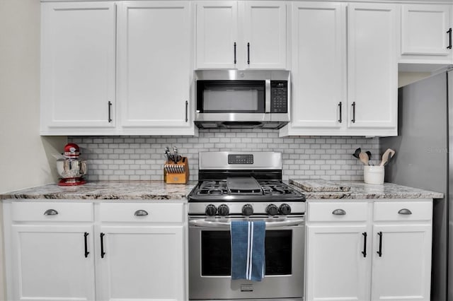 kitchen featuring decorative backsplash, stainless steel appliances, white cabinets, and light stone countertops