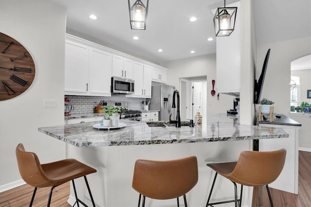 kitchen with kitchen peninsula, light hardwood / wood-style floors, decorative light fixtures, white cabinets, and appliances with stainless steel finishes