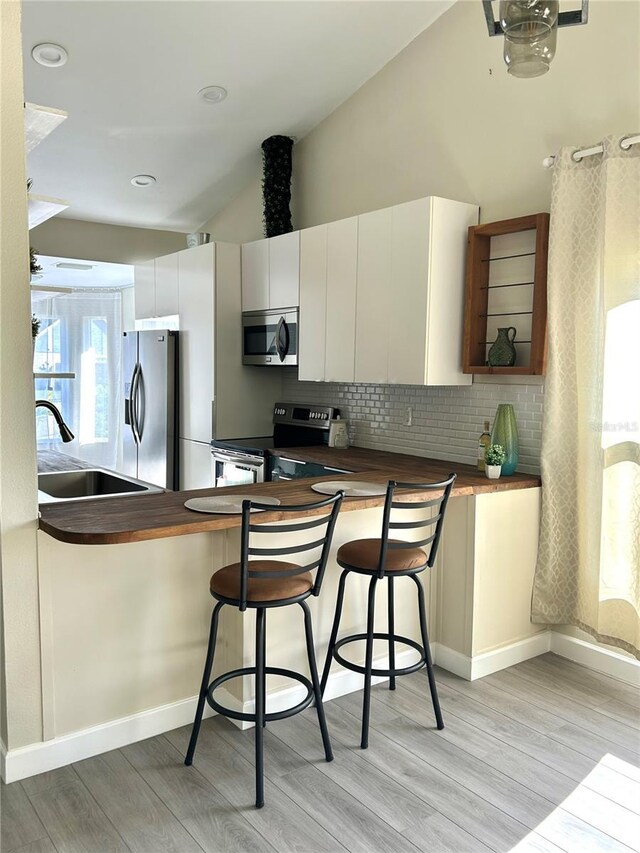 kitchen featuring wood counters, a breakfast bar, stainless steel appliances, vaulted ceiling, and white cabinets