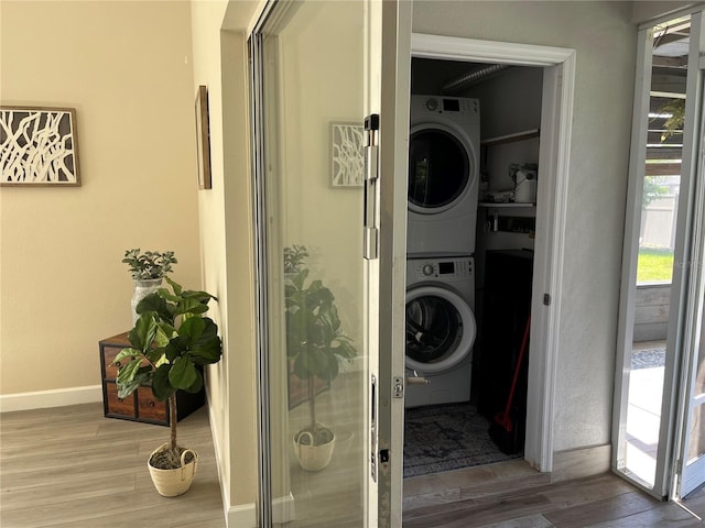 clothes washing area featuring stacked washing maching and dryer and wood-type flooring