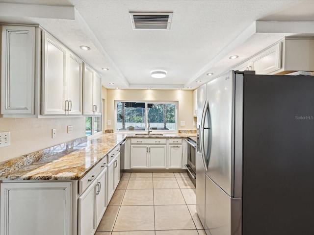 kitchen featuring light tile patterned floors, light stone counters, plenty of natural light, white cabinets, and appliances with stainless steel finishes