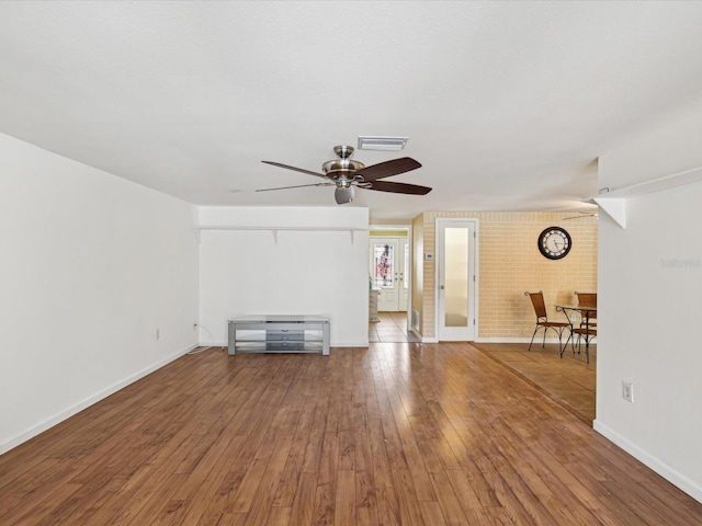 unfurnished living room featuring ceiling fan, brick wall, and hardwood / wood-style flooring