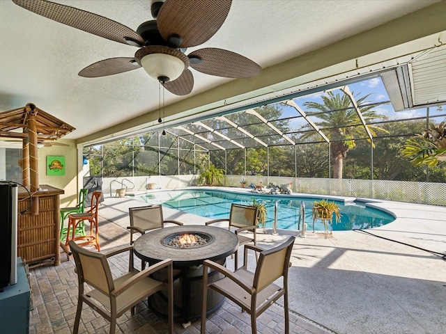 view of swimming pool with glass enclosure, ceiling fan, a patio, and a fire pit